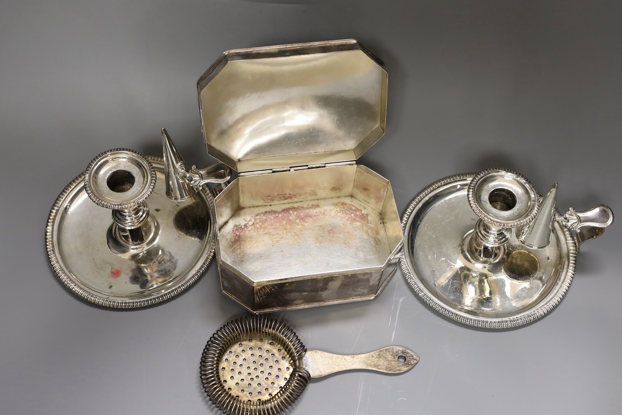 A pair of silver plated chambersticks, a plated octagonal box and cover and a plated strainer.
